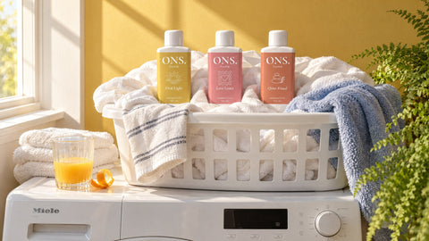 Drie flessen wasparfum van ONS. in een wasmand vol schone was in de ochtendzon: hoe lang ruikt wasparfum?